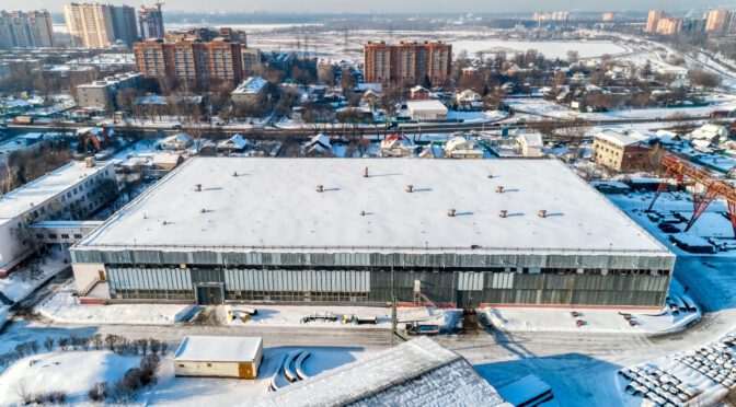 A large commercial warehouse with snow on the roof and surrounding areas.