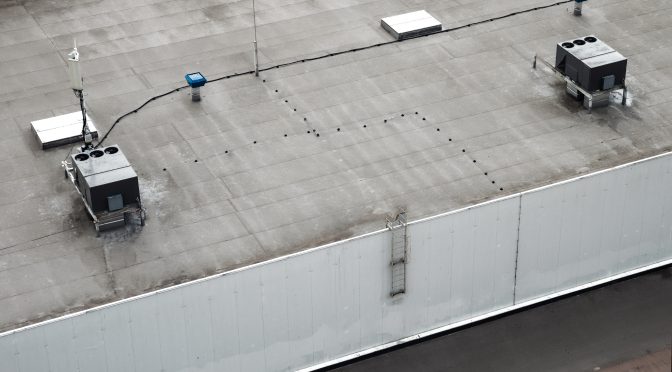 A commercial roof with wiring running across it, weaving through skylights and HVAC units.