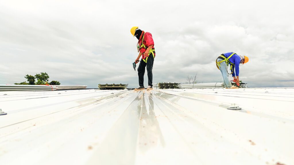On top of a commercial building, two workers install a new roof.