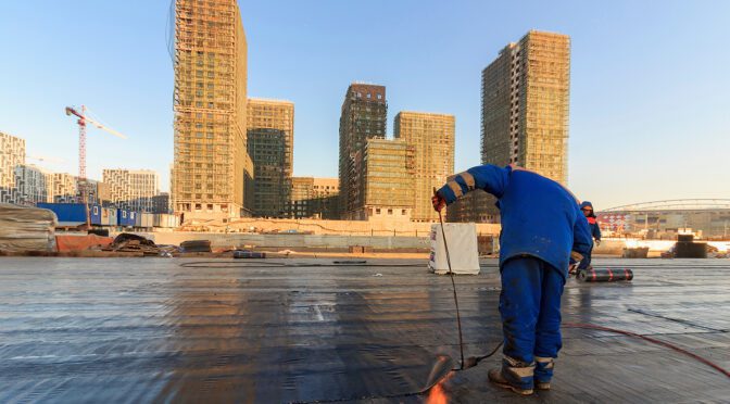 A roofing contractor uses a flame to melt sealant on a built-up roof
