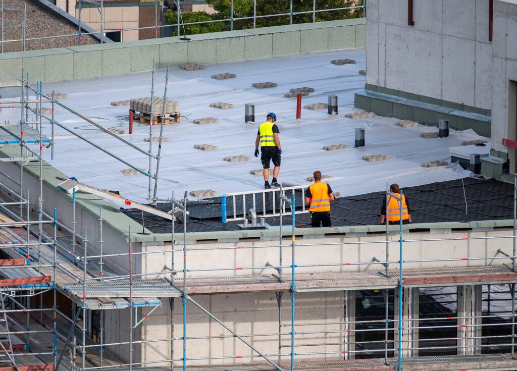 A trio of construction workers install roofing on a commercial building
