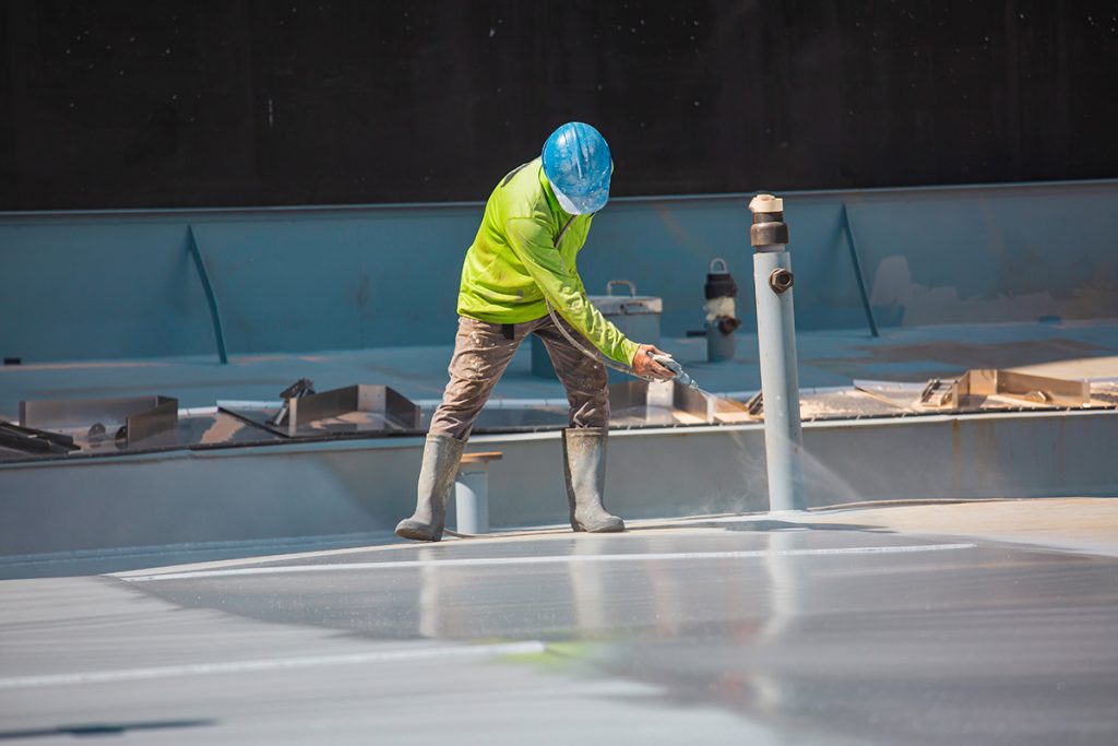 A contractor spraying a coating onto a low-slope roof