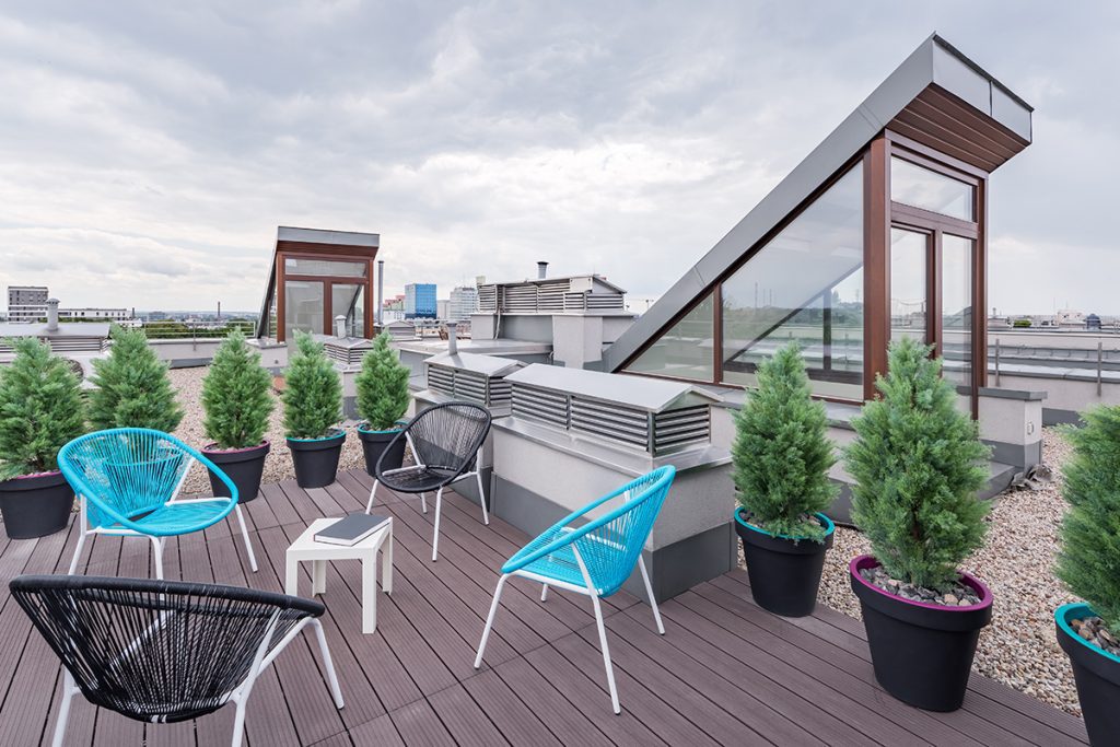 A rooftop space with small potted shrubs and four lounge chairs around a small table.