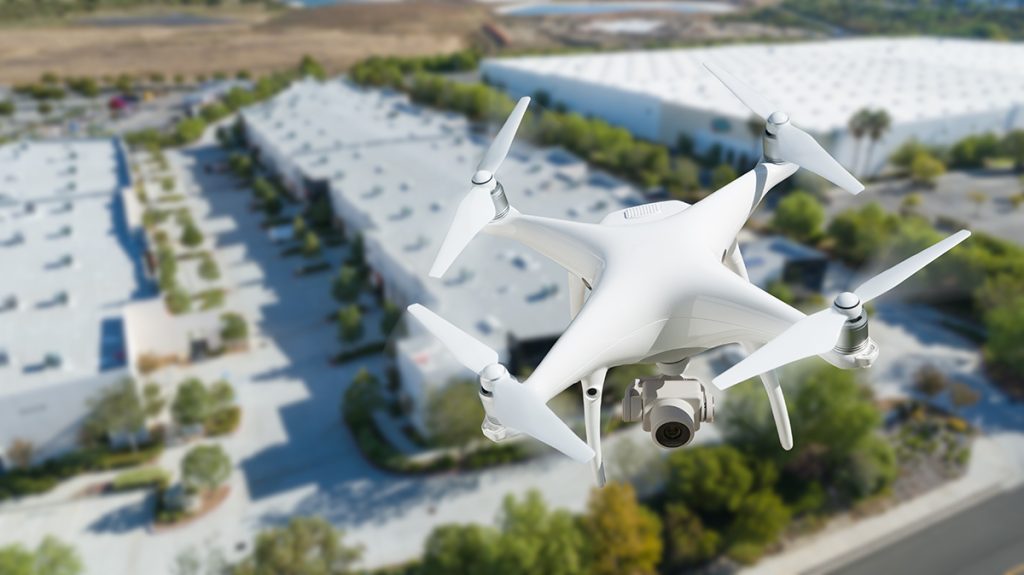 A closeup of a drone in flight with a row of commercial buildings in the distance below