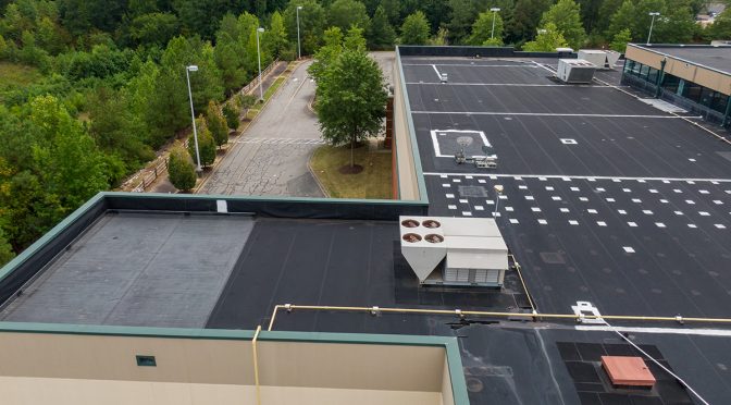 A drone view of a commercial roof, with a parking lot visible in the background.