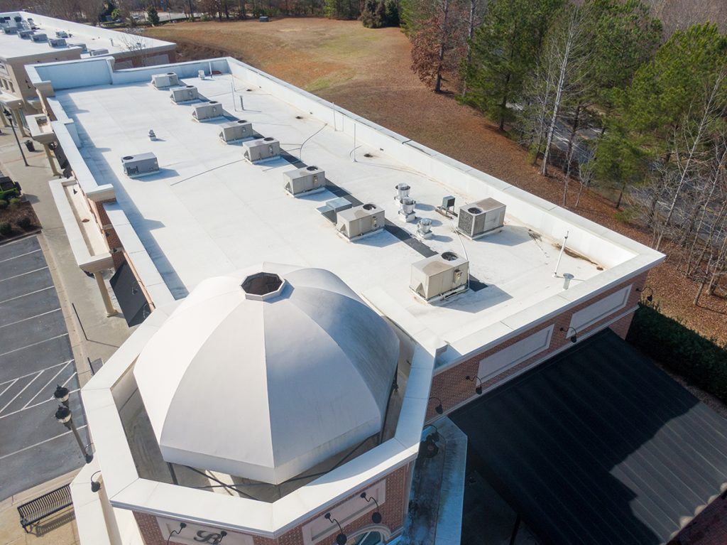 An overhead view of a white commercial building roof with a dome at the front end and multiple AC units lining the middle