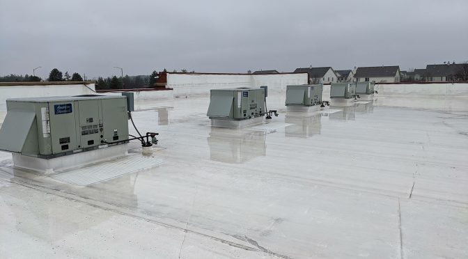 A row of HVAC boxes installed on a commercial roof covered by a sheen of water.