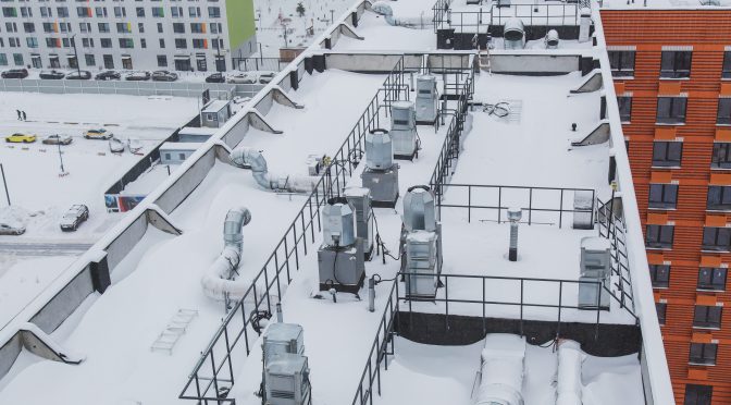 A bird's-eye view of a commercial roof with a robust HVAC and ducting system, as well as a central platform. The entire scene is covered in snow.